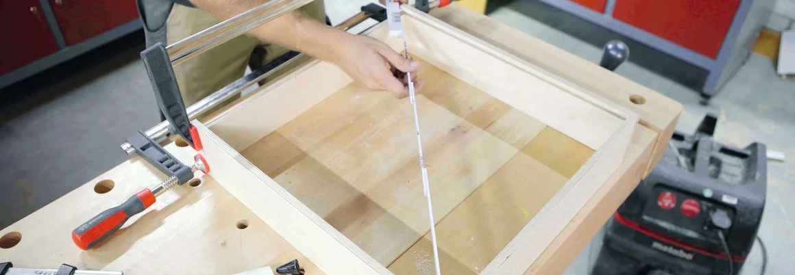 Person baut einen Holzrahmen mit Schraubzwingen zusammen.